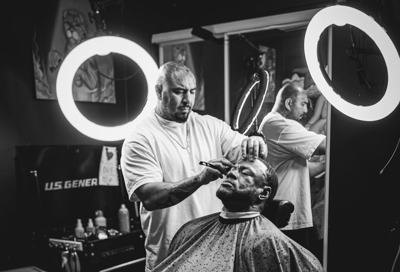 Lucky working a straight razor on a client's hairline between two ring lights in his shop.